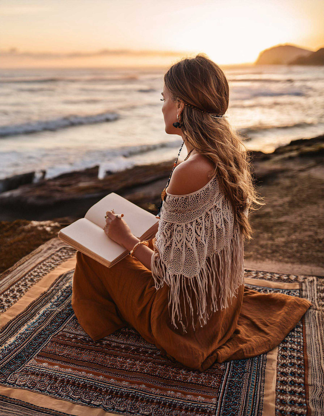 Woman sitting on the beach at sunset deep in contemplation as she writes her thoughts in to a journal