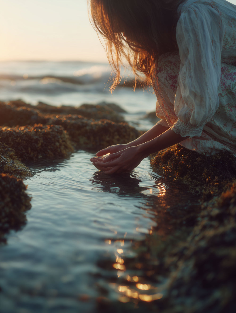 Cosmic Creator Stock Images: Woman crouched down at the edge of a rock pool in the afternoon golden light, spiritual coach stock images